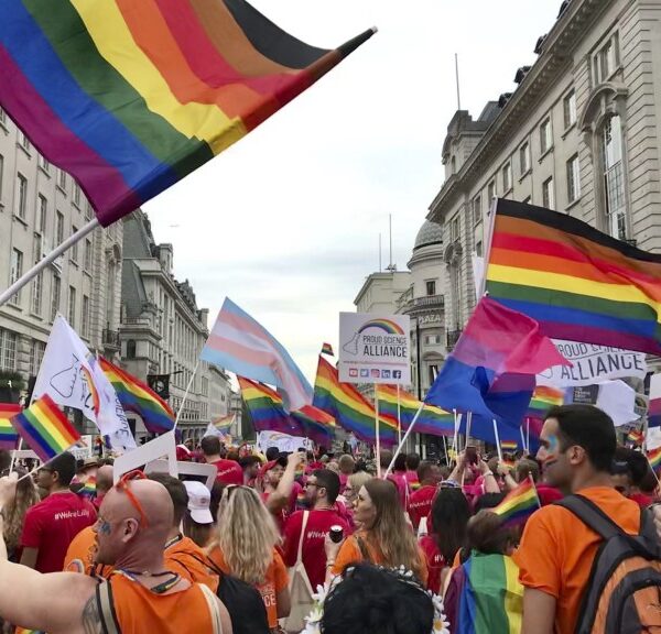 Group of people marching in London Pride Parage waving LGBTQ+ rainbow flags