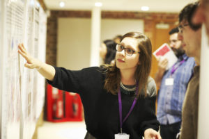 A person pointing to the ACSC poster, engaging onlookers in conversation