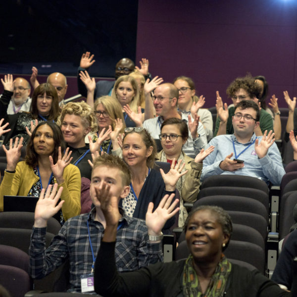 A group of peeople at the EDIs symposium waving their hands in a silent / BSL applause