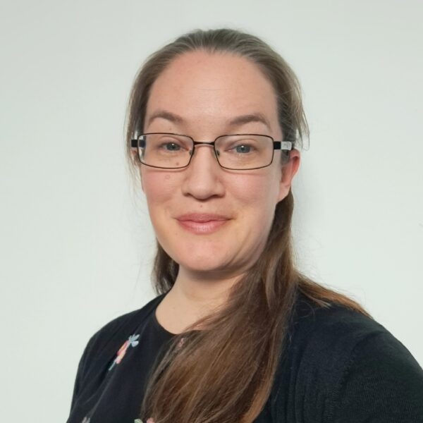 A photo of Sarah Jenner, a white woman with long brown hair and glasses smiling at the camera.