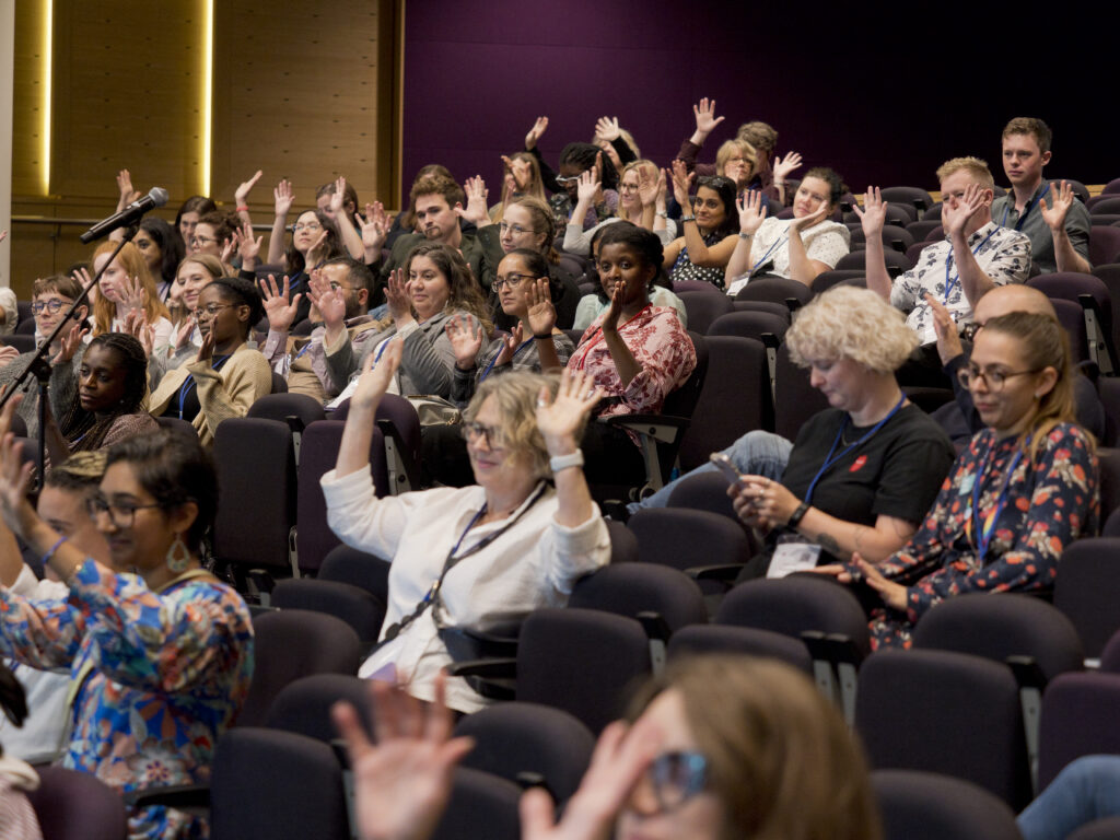 A photo of the audience at the EDIS Symposium engaging in "silent clapping" by waving their hands